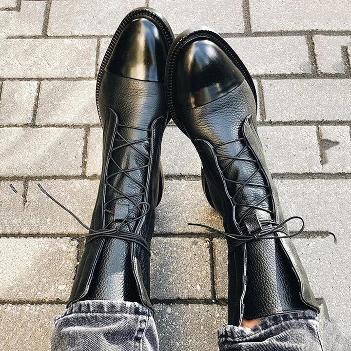 Black leather lace-up boots displayed on a brick surface.