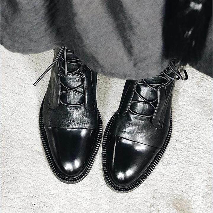 Close-up of black leather lace-up boots worn with gray pants.
