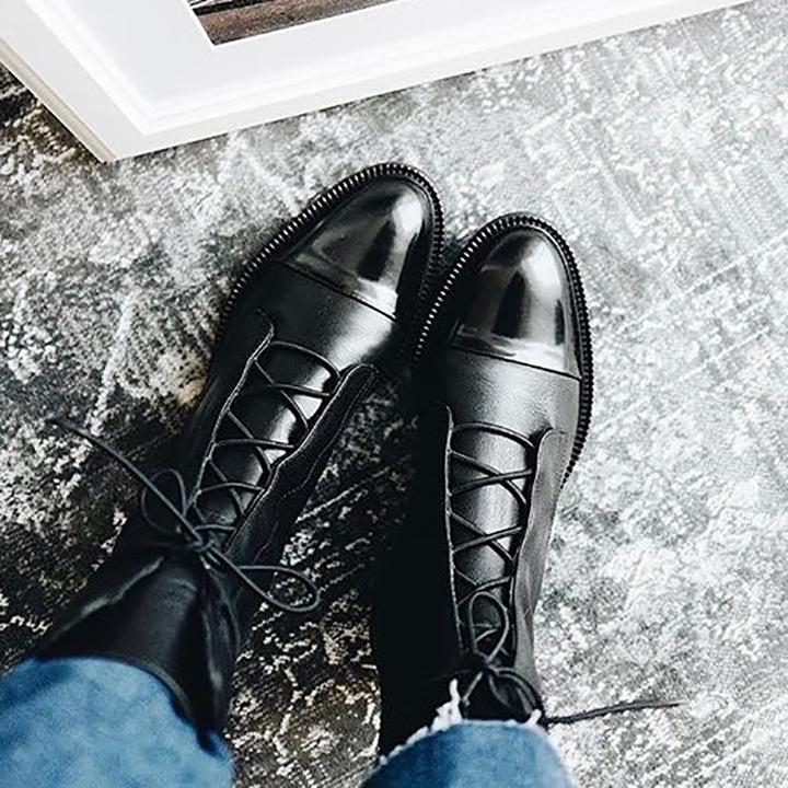 Black leather lace-up boots with gold-tone hardware displayed on a patterned surface.