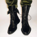 Black leather lace-up ankle boots with low heels and rounded toes, worn with green pants.