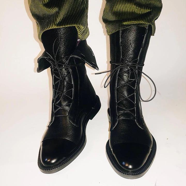 Black leather lace-up ankle boots with low heels and rounded toes, worn with green pants.