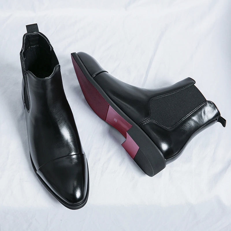 Black leather Chelsea boots displayed with one boot showing its burgundy-colored sole and heel detail.