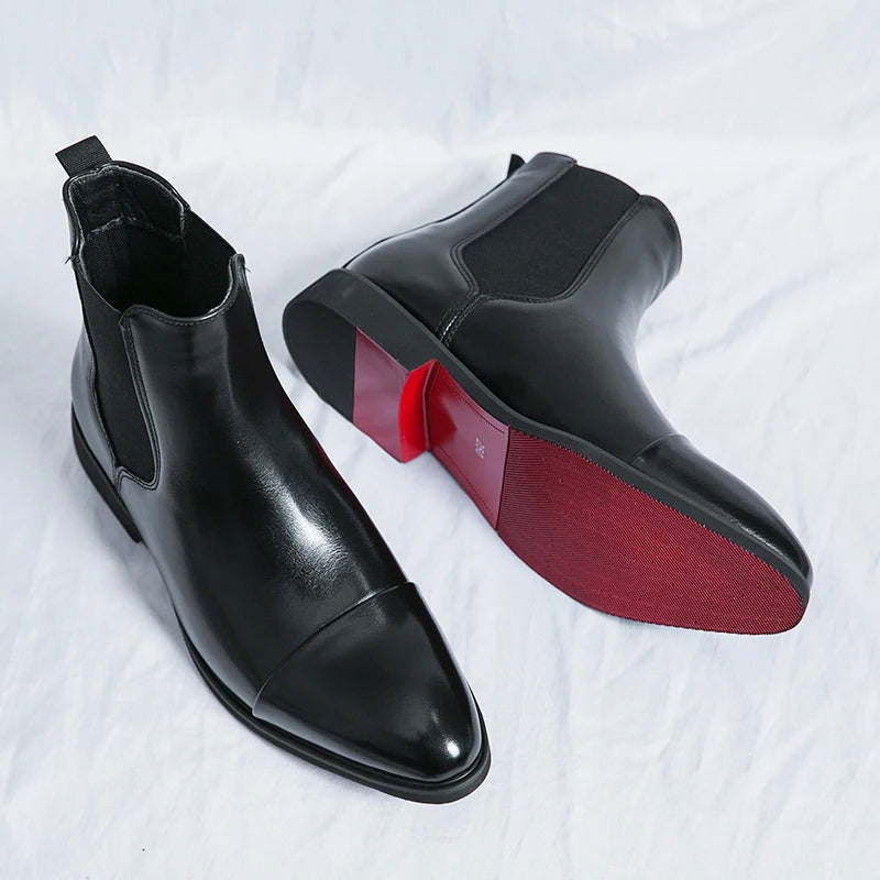 Pair of black leather Chelsea boots displayed with one boot showing its burgundy-colored sole, highlighting the sleek pointed design.