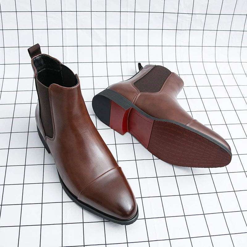 Pair of brown leather Chelsea boots with elastic side panels, pull tabs, pointed toes, and low block heels displayed on a grid background.