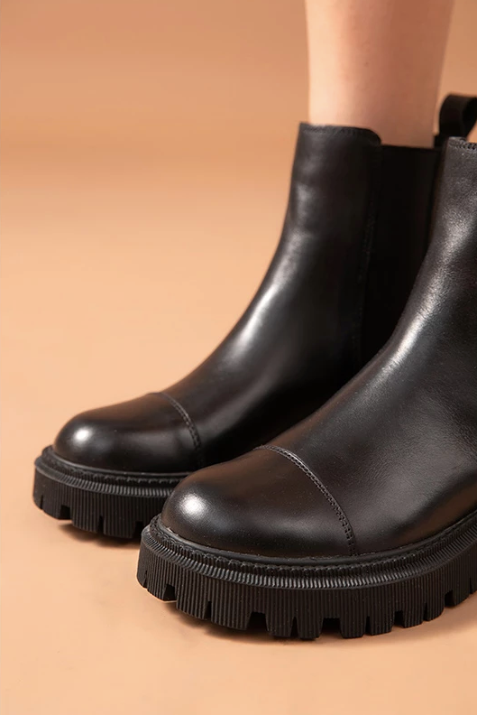 Close-up of black leather Chelsea ankle boots for women showing the cap-toe seam and chunky lug sole