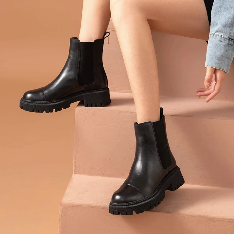 Woman on steps wearing black leather Chelsea ankle boots with cropped jeans, showing the two-inch square heel