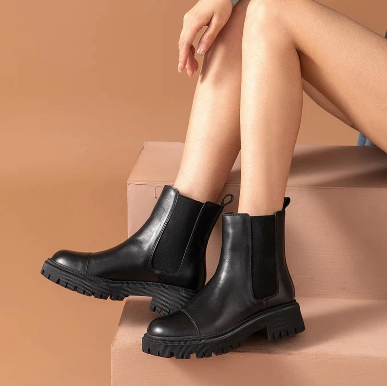 Seated woman wearing black leather Chelsea ankle boots for women with elastic side panels and lug sole