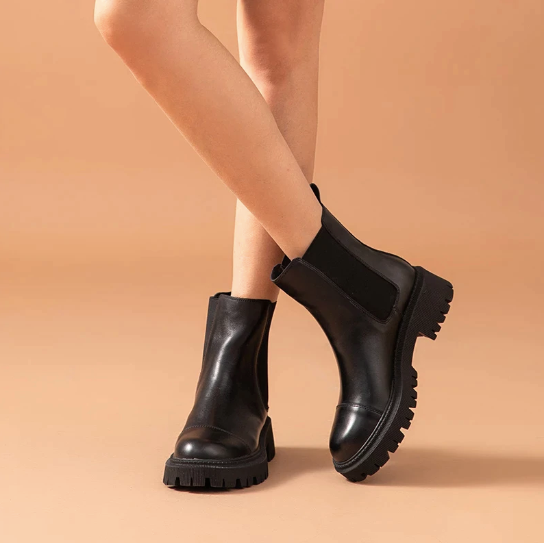 Black leather Chelsea ankle boots for women worn with bare legs, side view showing the square heel height