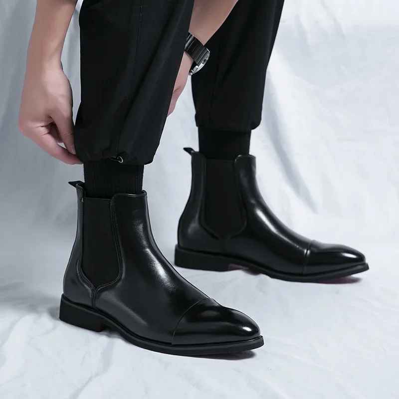 Close-up of black leather cap-toe Chelsea boots worn with black trousers, showing elastic side panels and low block heel