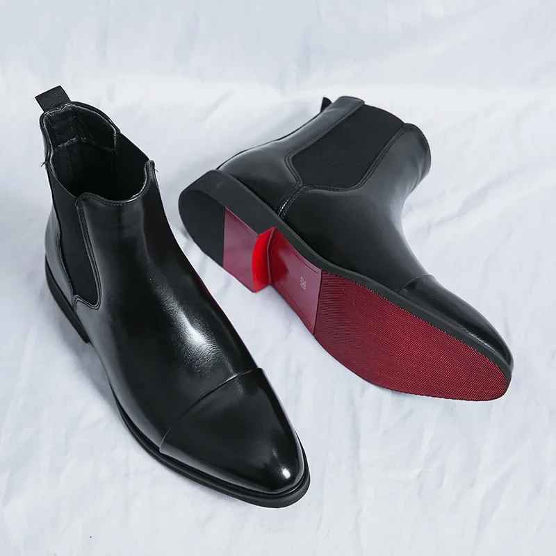 Pair of black cap-toe leather Chelsea boots laid on white fabric, one tilted to show the red textured sole