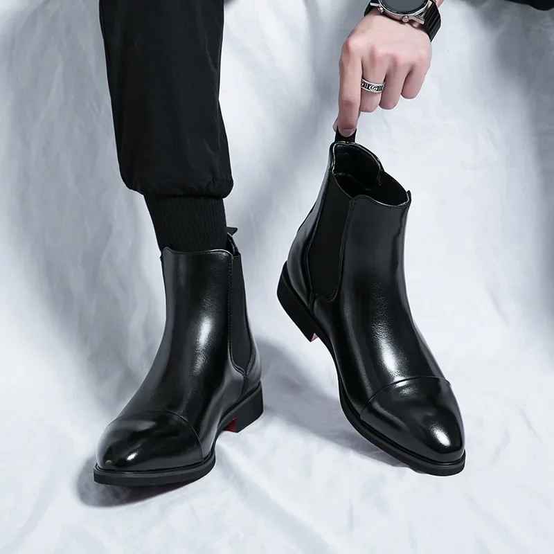 Man pulling on a black leather cap-toe Chelsea boot by the heel tab, worn with black trousers and socks