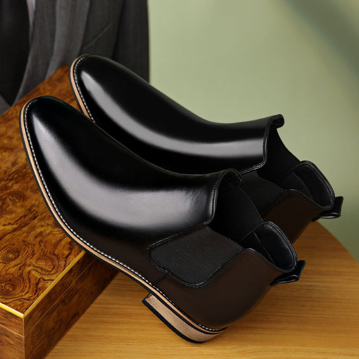 Pair of black Chelsea boots displayed on a wooden surface, showing the elastic panels and pointed toes.