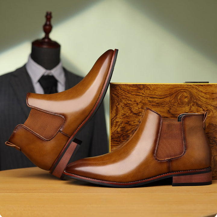 Brown leather Chelsea boots displayed on a wooden surface with a tailored suit in the background.