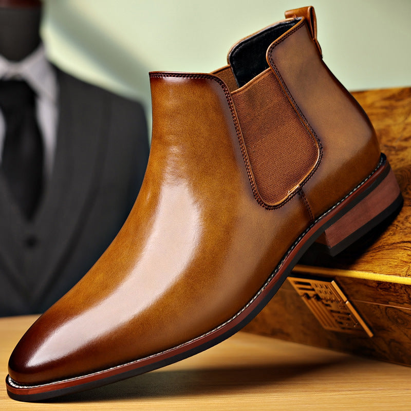 Polished brown leather Chelsea boot with elastic side panels, pull tabs, pointed toe, and low stacked heel displayed on a wooden surface.