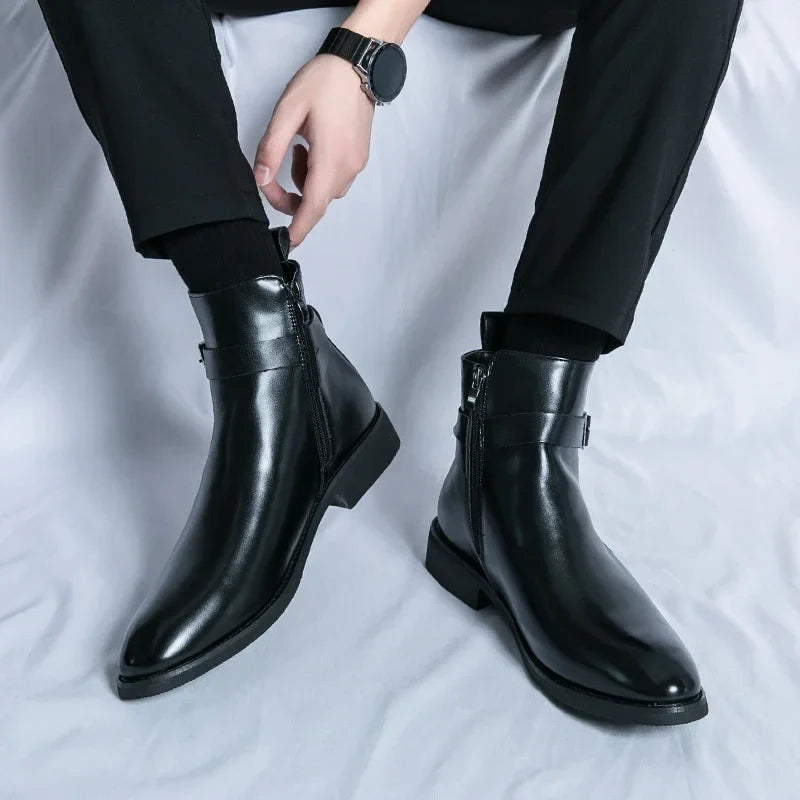Person wearing polished black leather ankle boots with side buckles, pull tabs, pointed toes, and block heels.