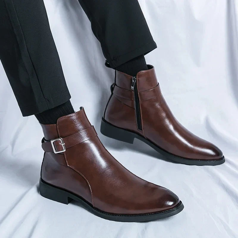 Close-up of dark brown ankle boots with side buckles and pointed toes, worn with dark trousers.