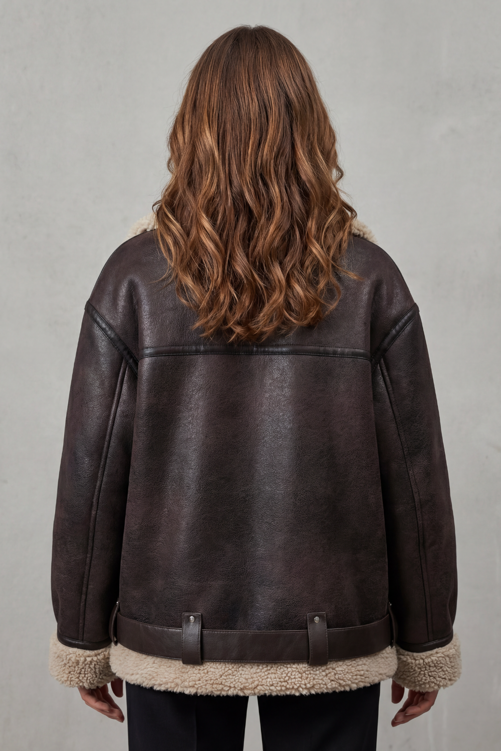 A woman wearing a dark brown leather shearling aviator jacket with a belted waist, shown from the back