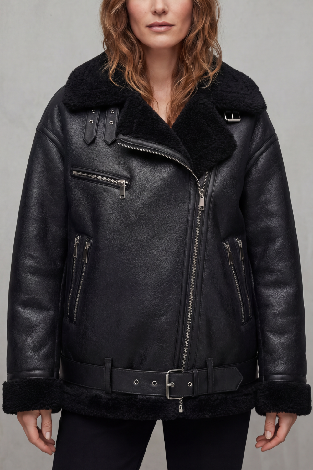 A woman wearing a black leather shearling aviator jacket with a belted waist, zip front, and plush shearling collar