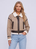 A woman wearing a beige leather shearling aviator jacket with a cropped fit, shearling collar, zip front, and belted waist