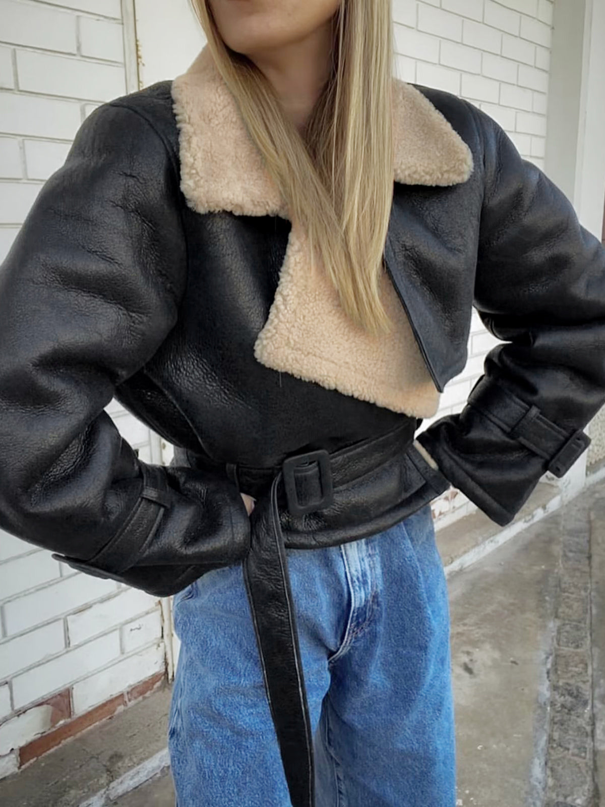 A woman wearing a black leather shearling aviator jacket with a cropped fit and buckled cuffs, shown from the side