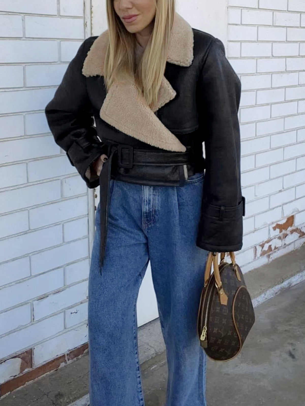 A woman wearing a black leather shearling aviator jacket with a cropped fit and buckled cuffs, shown outdoors