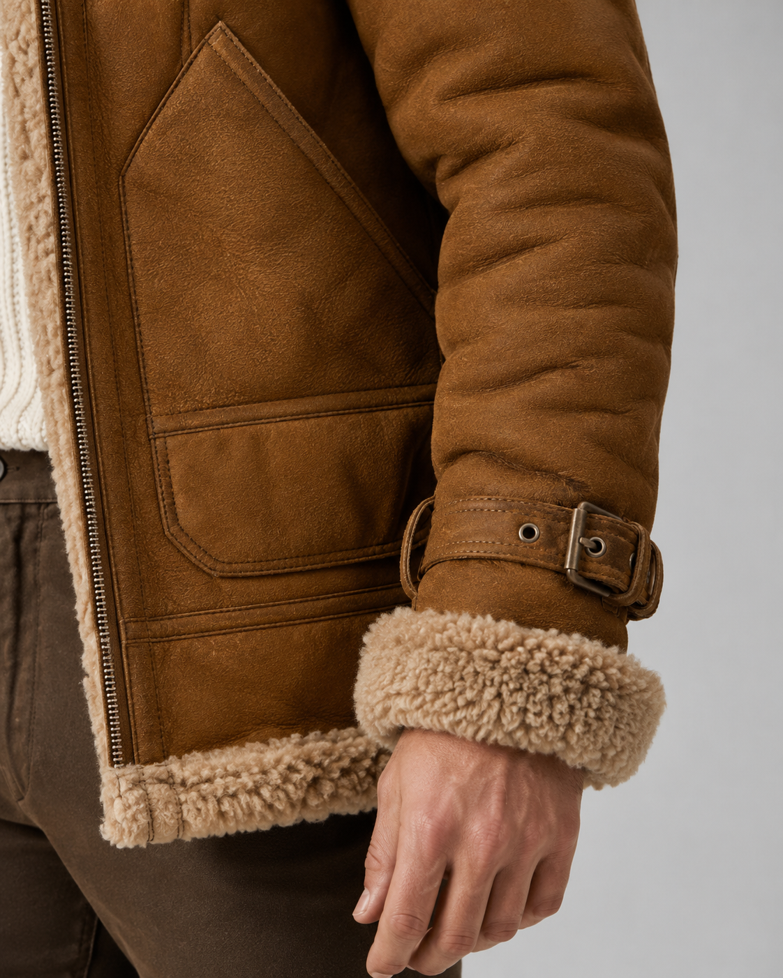 Brown leather shearling aviator jacket close-up showing the patch pocket, buckle cuff, thick shell, and plush lining