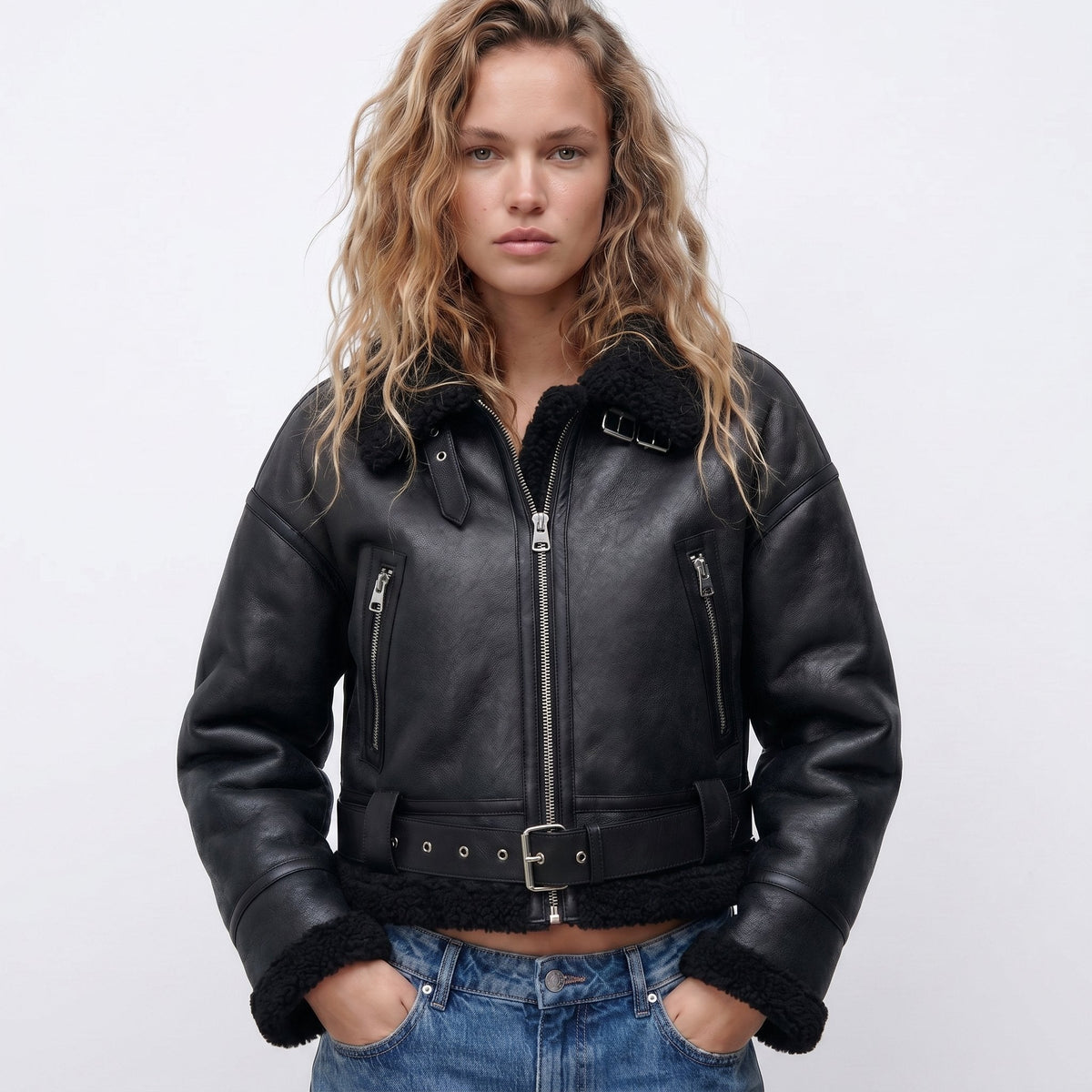 Black leather shearling bomber jacket worn by a female model, featuring cropped fit, shearling trim, and zip pockets