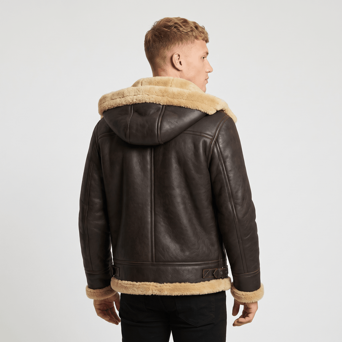 A man wearing a dark brown leather shearling jacket with a hood, plush lining, and button closure, shown from the back