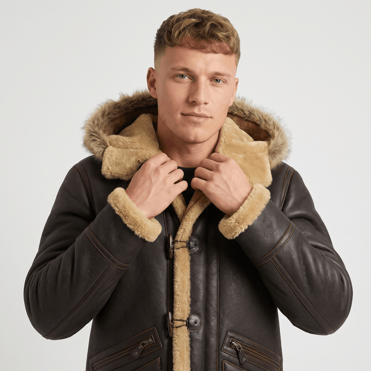 Close-up of a man wearing a dark brown leather shearling jacket, showing the plush-lined hood and button closure