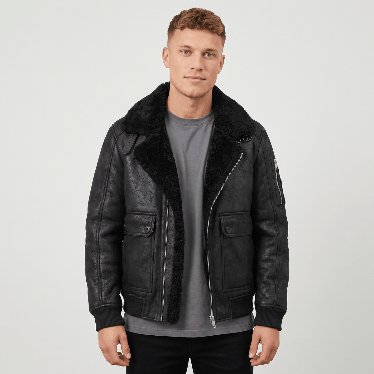 A man wearing a black leather shearling jacket with plush lining, a full-zip front, and a shearling collar, standing outdoors