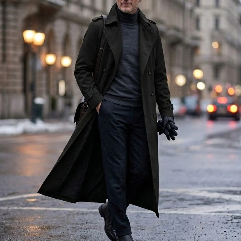 A man wearing a black long double-breasted trench coat with an adjustable belt and tailored profile, walking on a city street