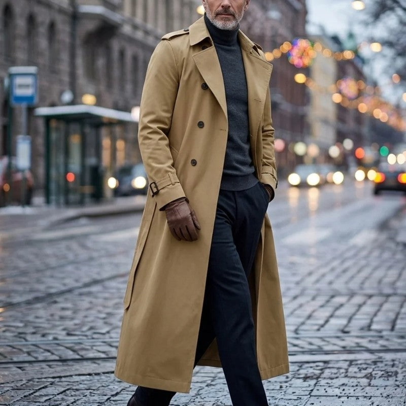 A man wearing a tan long double-breasted trench coat with an adjustable belt and tailored profile, walking on a city street