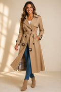 A woman wearing a beige long double-breasted trench coat with a belted waist and plaid lining