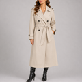 A woman wearing a cream long trench coat with a double-breasted front, belted waist, and longline fit