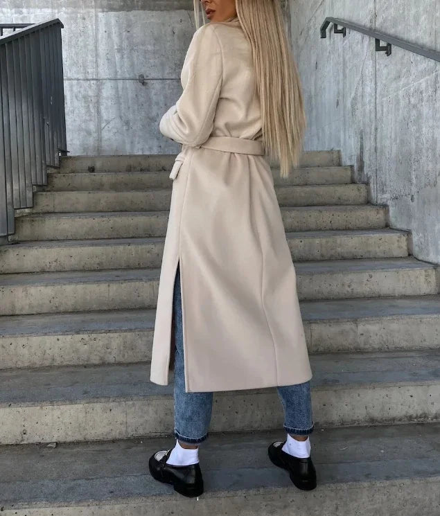 A woman wearing a white long double-breasted trench coat with a belted waist, shown from the back