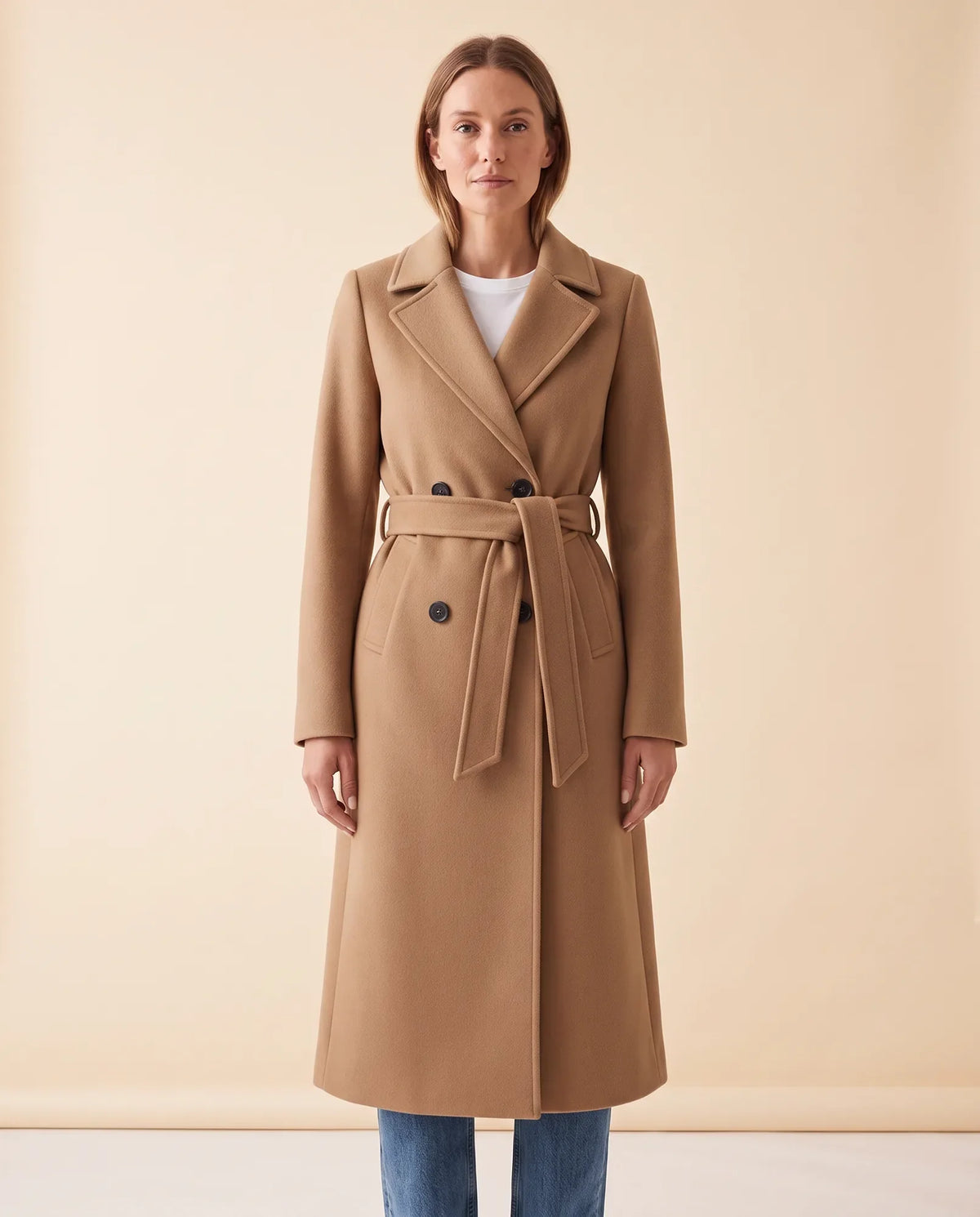 A woman wearing a camel longline belted coat with a double-breasted front and notched lapel