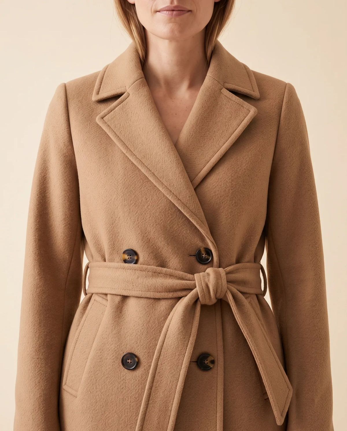 Close-up of a camel longline belted coat showing the notched lapel, double-breasted front, and waist belt