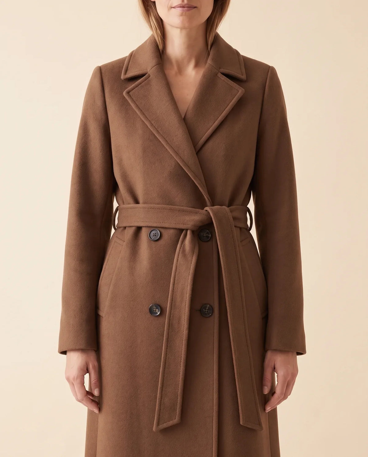Close-up of a brown longline belted coat showing the double-breasted front, notched lapel, and waist belt