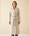 A woman wearing a cream longline belted coat with a double-breasted front and notched lapel