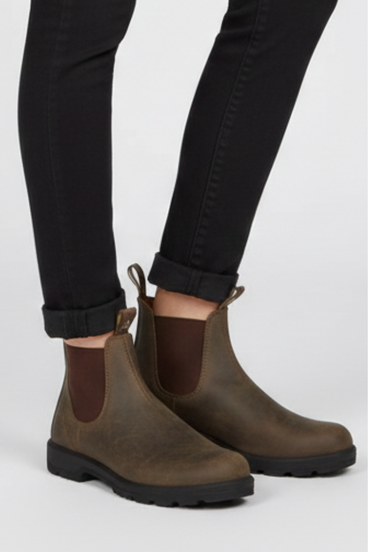 Rustic brown lug sole Chelsea boots for women worn with cuffed black jeans, showing the front pull tab