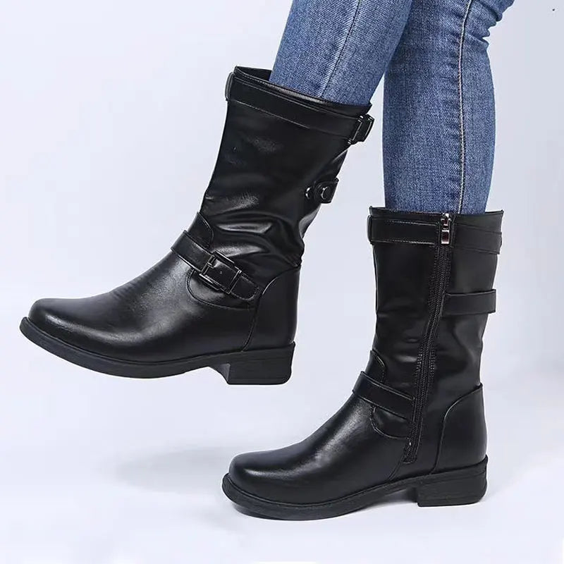 Black knee-high boots with buckle details and low heels worn with blue jeans.