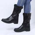 Black knee-high riding boots with buckle straps and low block heels worn with blue jeans.
