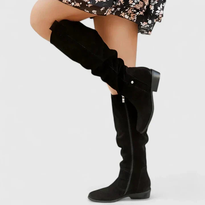 Black suede over-the-knee boots with a slouchy shaft, side zip, snap tab detail, and a low block heel.