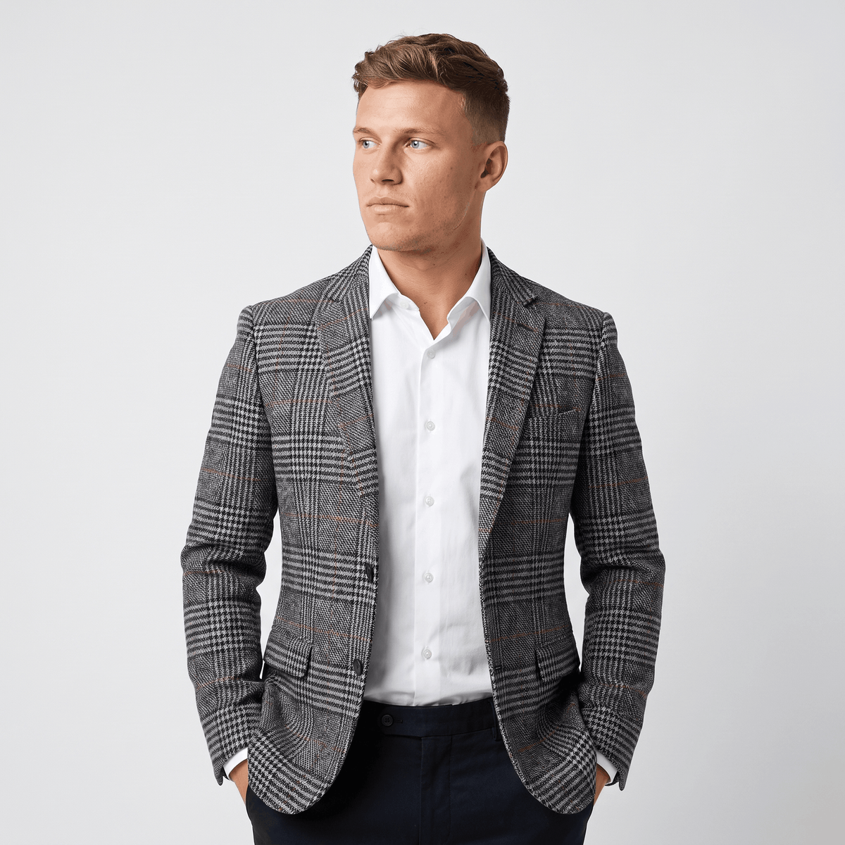 Man wearing a charcoal gray plaid tweed blazer over a white dress shirt with a tailored fit and classic notched lapel.