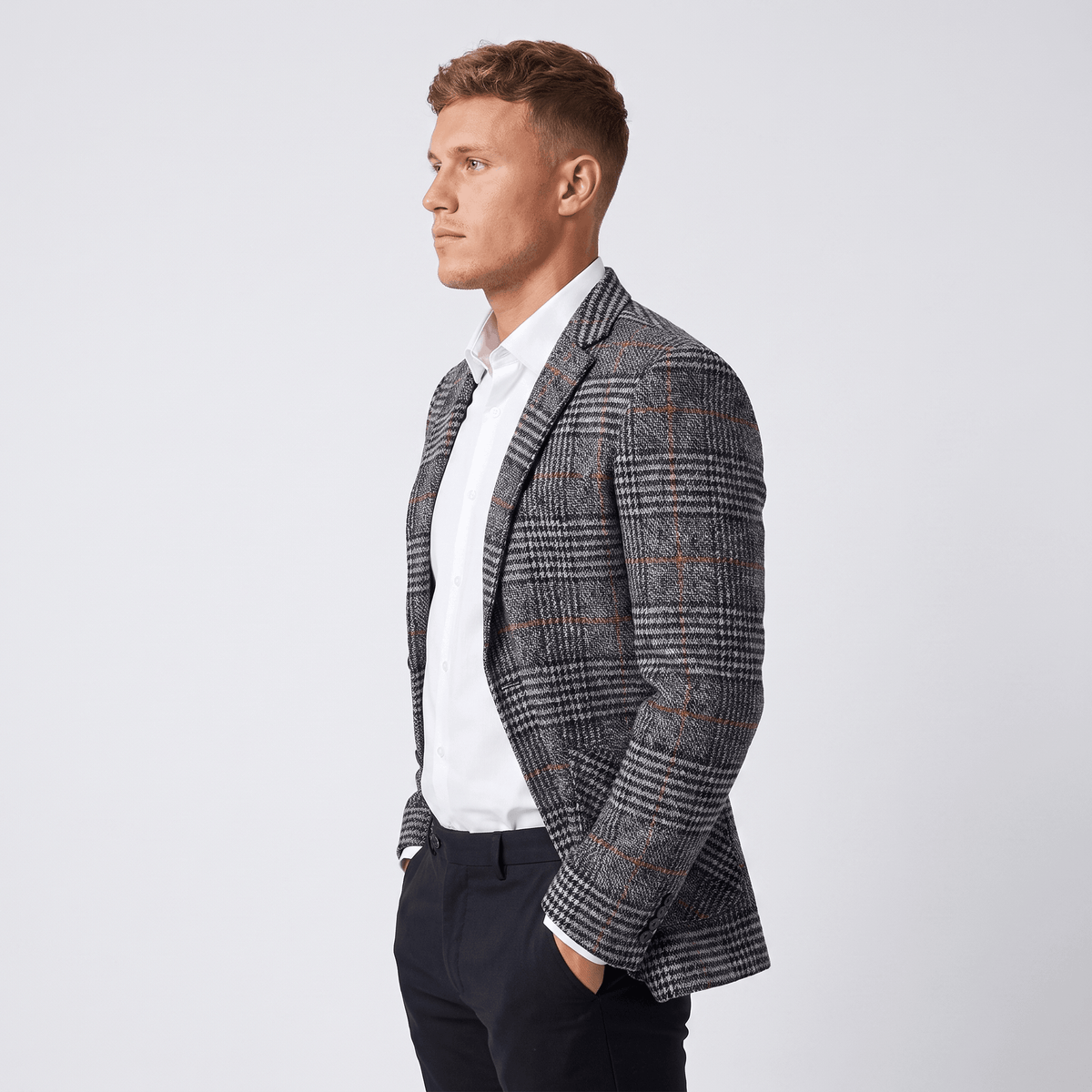 Side view of a man wearing a charcoal gray plaid tweed blazer with a notched lapel and tailored silhouette.