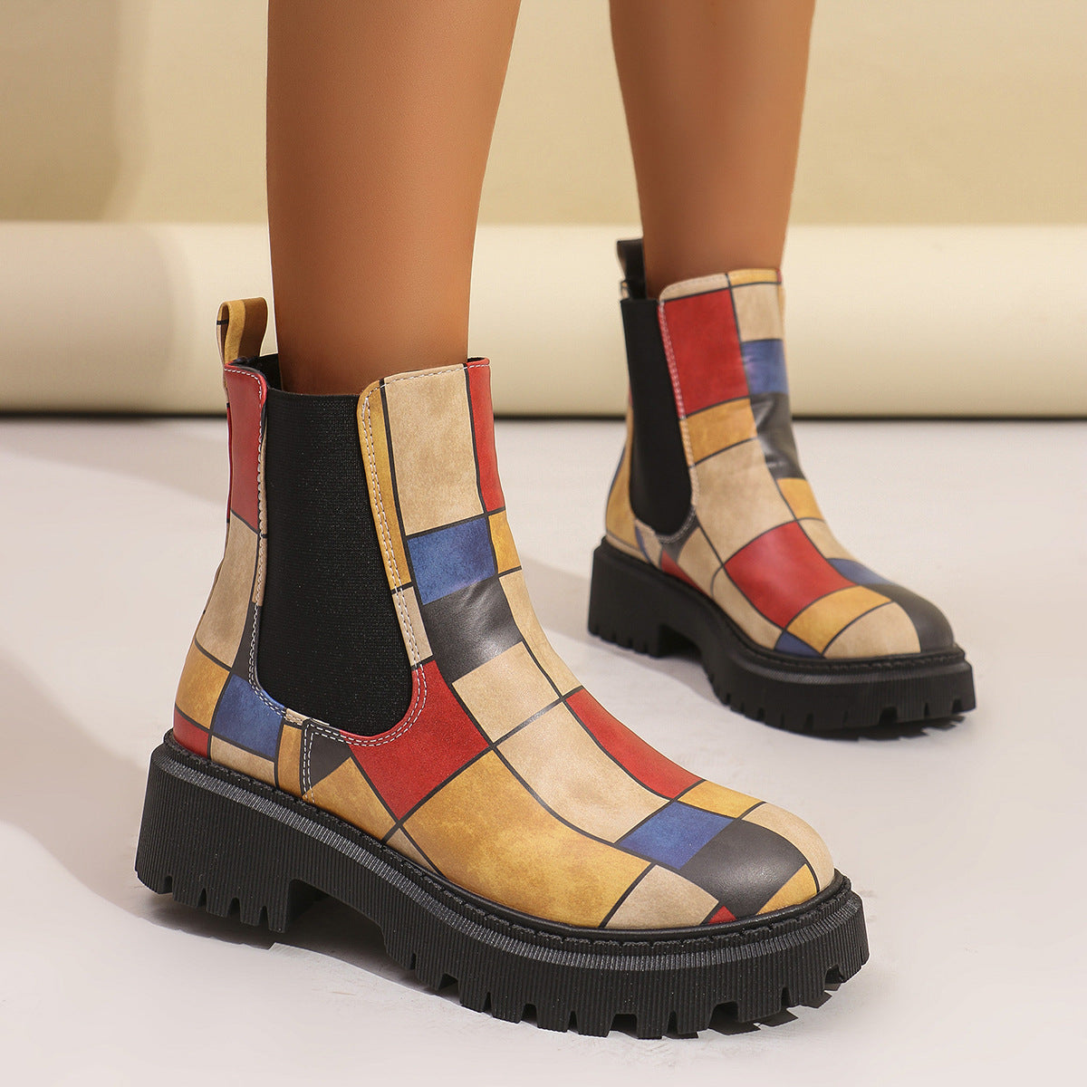 Woman wearing red and tan geometric panel platform Chelsea boots with black elastic side panels and lug sole