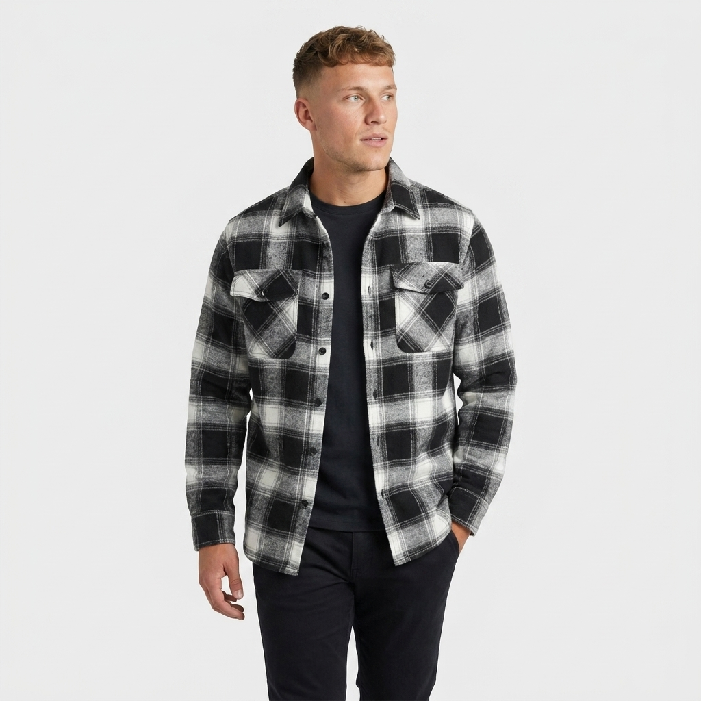 Man wearing a black and white plaid overshirt jacket with a button-front closure, chest pockets, and long sleeves over a dark shirt.