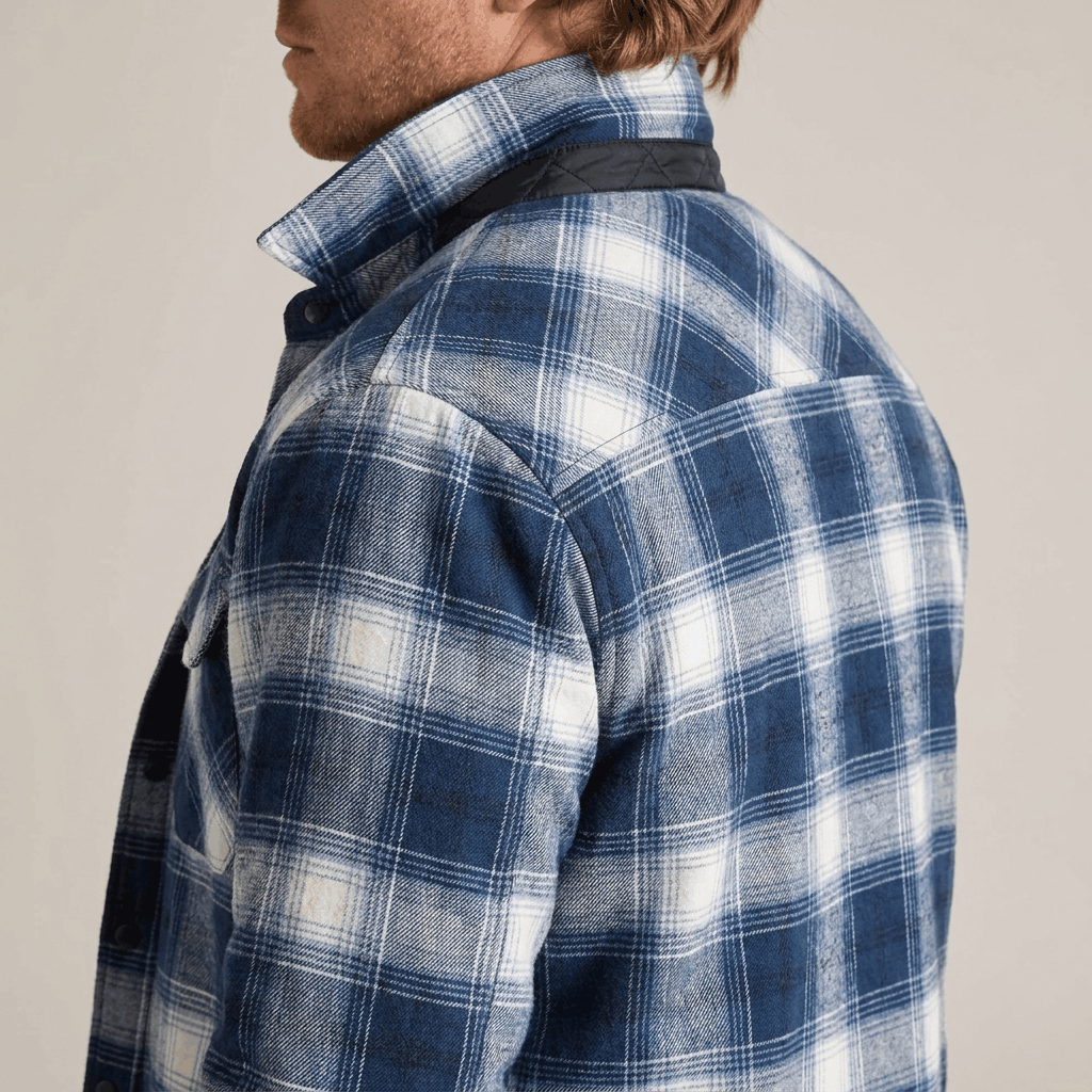 Close-up side view of a blue and white plaid quilted-lined overshirt jacket showing the textured plaid fabric and collar.