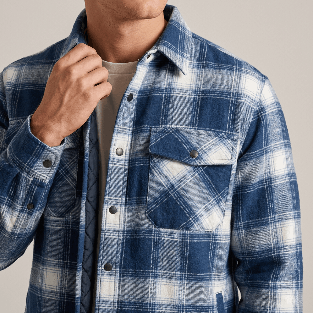 Close-up of a man wearing a blue and white plaid quilted jacket with a button-front closure, pointed collar, chest pockets, and textured quilted fabric.