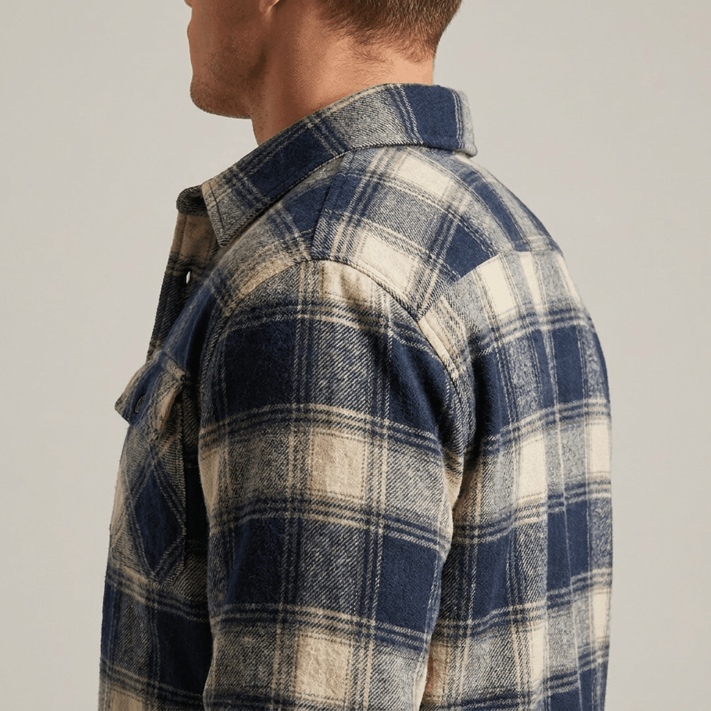 Man wearing a blue and cream plaid quilted-lined overshirt jacket with dark trousers and white sneakers in a studio setting.